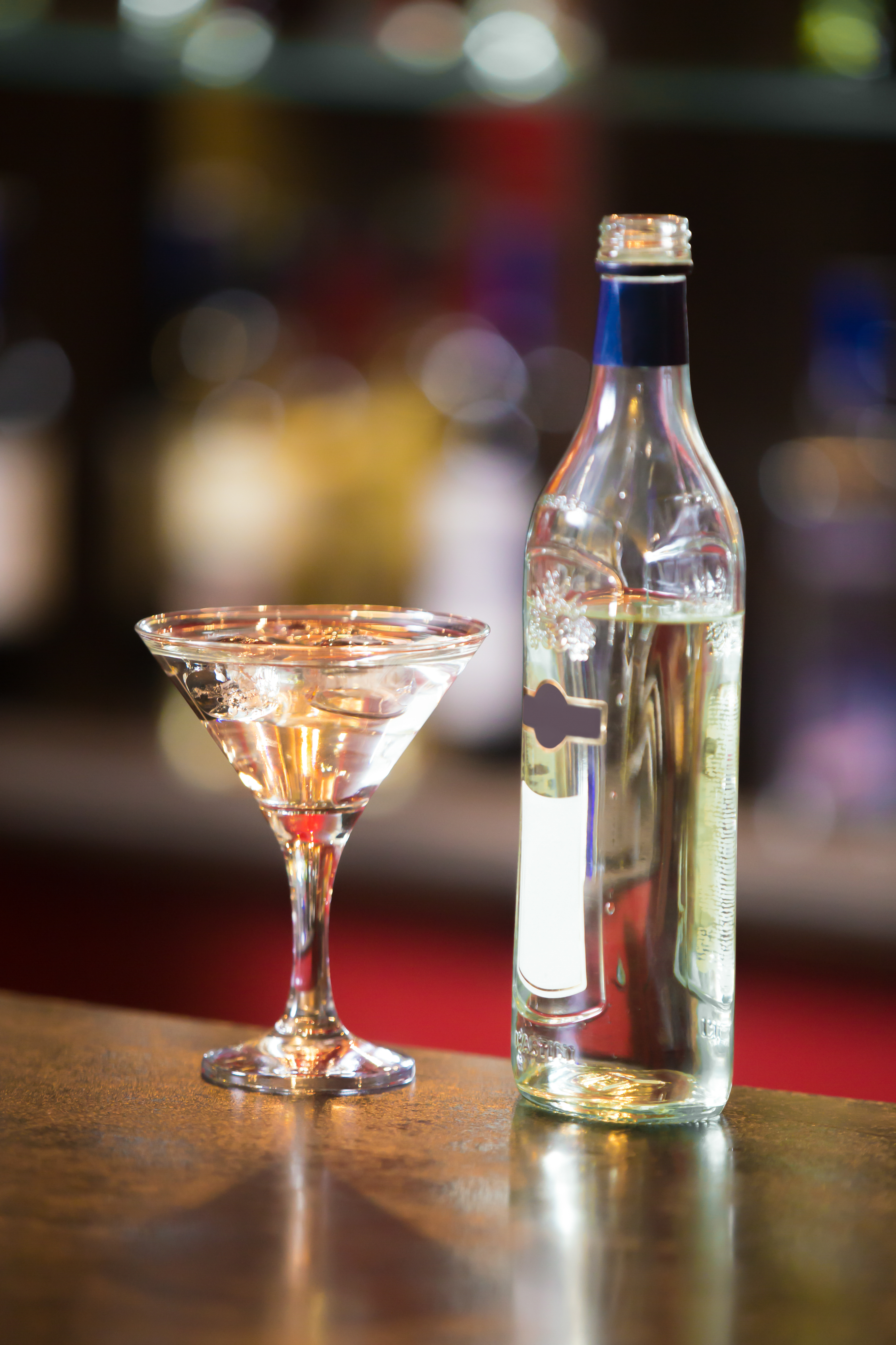 Bottle and Alcoholic drink with ice cubes and olive in martini glass on bar counter